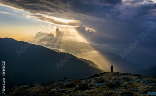 A conceptual image of a man being hopeful, positive and optimistic. A person looking at a beam of sun rays in a dark and moody atmosphere. Sunset in Langtang National Park, Nepal on Gosainkunda trail.