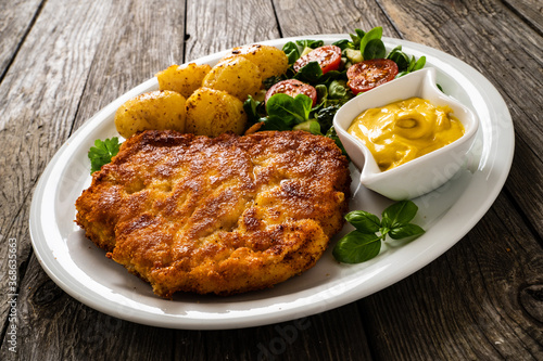 Breaded pork chop with boiled potatoes and vegetable salad on wooden background 