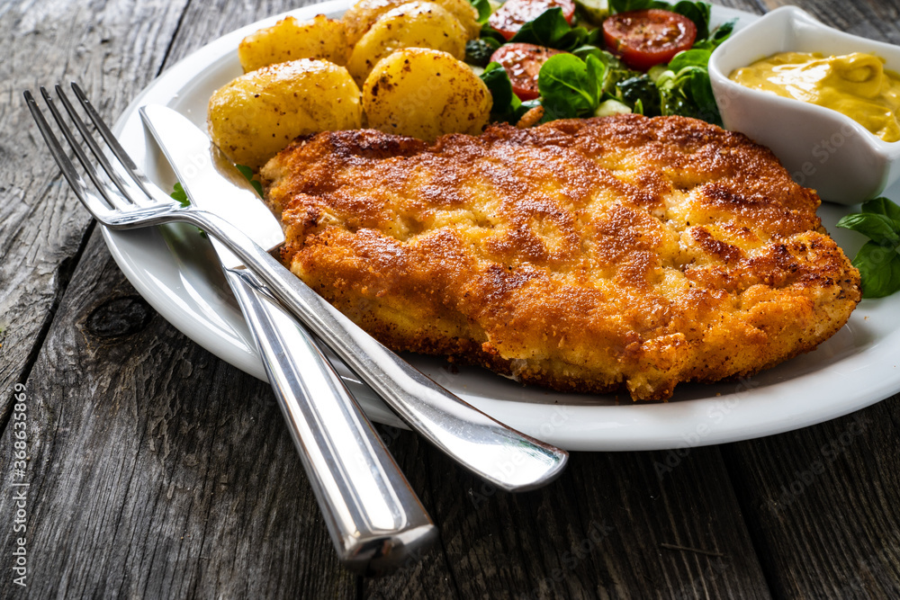 Breaded pork chop with boiled potatoes and vegetable salad on wooden background
Breaded pork chop with boiled potatoes and vegetable salad on wooden background