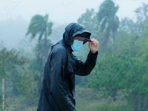 Man wears face mask and raincoat under heavy tropical rain. Tropical environment.