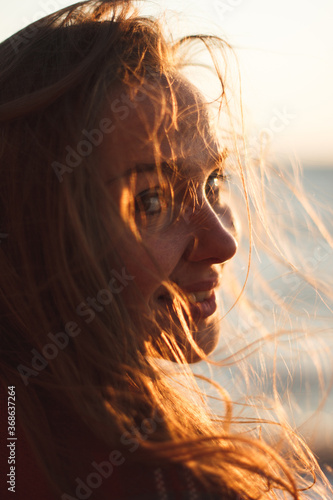 Portrait of a beautiful girl close-up. The hair of a beautiful girl gilded in the setting rays of the sun. Outdoors portrait at the seaside. Backlight and glare. Profile of an attractive young woman.