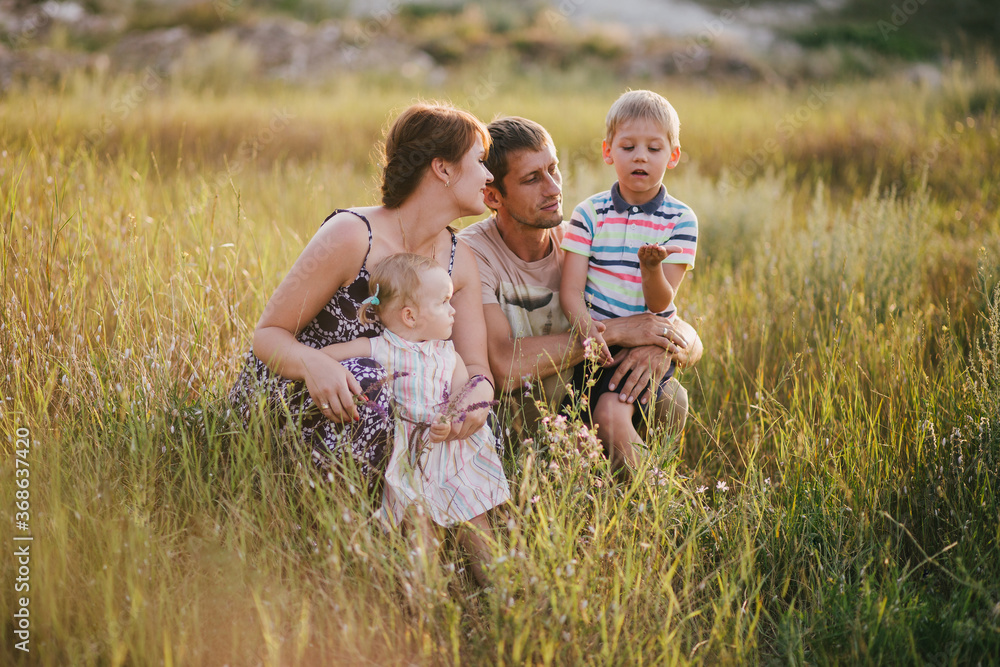Fototapeta premium Happy family of young parents and their little children walking in a field at sunset.