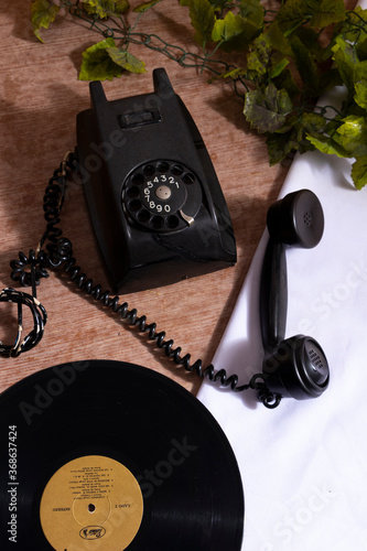 Telefono antiguo sobre mesa de madera con mantel blanco y platas verdes artificiales.  Antigedad negra sobre una mesa photo
