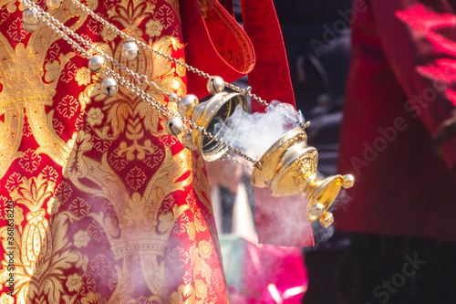 Billede på lærred A smoking censer in the hand of an Orthodox priest, against the background of a red brocade vestment embroidered with gold, in motion during the procession on Easter