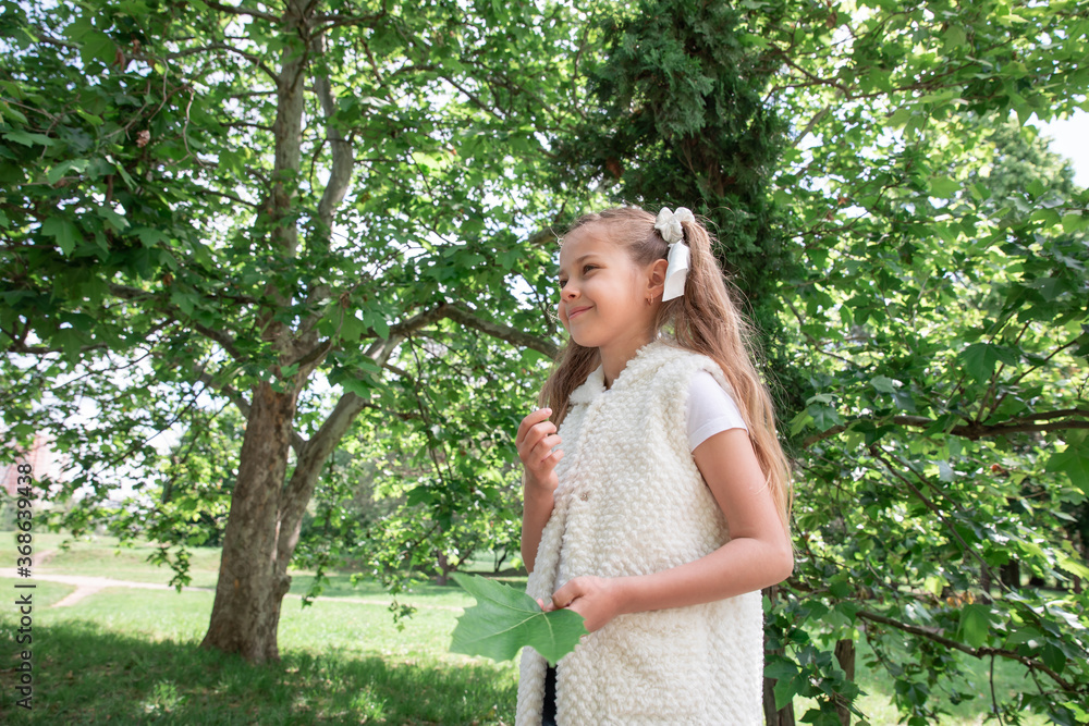 little girl with tails in green forest, in the park. The child smiles and holds a leaf. little girl with tails in green forest, in the park. The child smiles and holds a leaf.