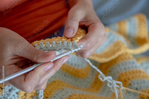 Needlework. Women's hands close up crocheting children's plaid. Crochet hook