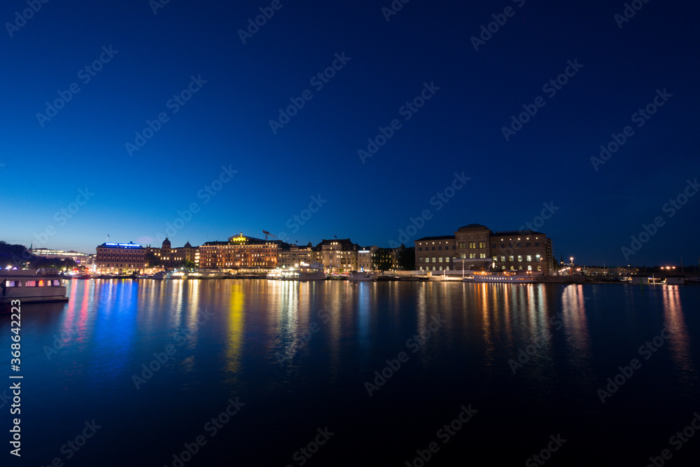 Illuminated skyline of the swedish city of Stockholm taken at night, the lights reflecting in the harbor's water.