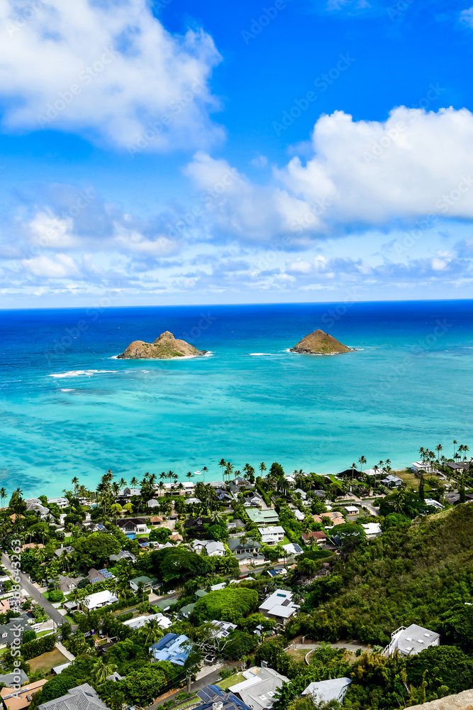 A photo from a mountain top in Oahu. Light blue ocean water seen in the distance and two small islands. Blue cloudy sky A photo from a mountain top in Oahu. Light blue ocean water seen in the distance and two small islands. Blue cloudy sky