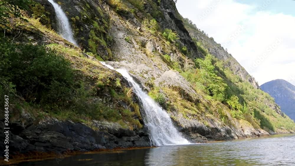 Waterfall falling, norwegian fjord Aurlandsfjord water mirror reflection. Bright view on wild mountains nature of Norway. Sunny travel day video. Waterfall falling, norwegian fjord Aurlandsfjord water mirror reflection. Bright view on wild mountains nature of Norway. Sunny travel day video.