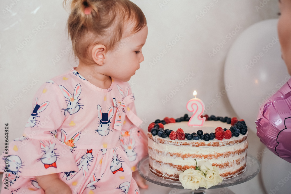 
Beautiful little girl in a dress with balloons. Little girl 2 years old in a pink dress with cake and balloons for her birthday