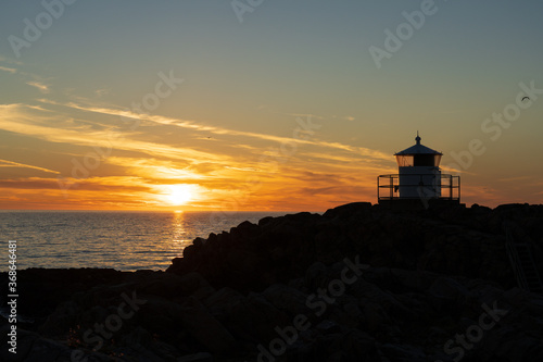 Lighthouse in silhouette with sunset over sea at Kullaberg nature reserve in Sweden. Popular tourist destination.