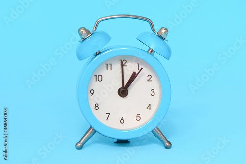 Blue alarm clock on blue background close up. 1 a.m., 1 p.m. Time concept.