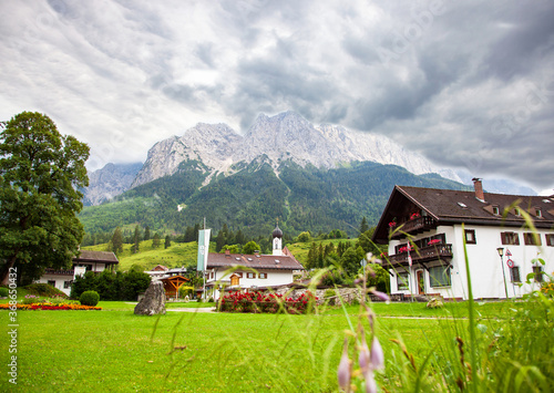Mountain panorama in front of cloud sky scene. Grainau, bavarian alps village against cloudy Sky. domed church with Mountains (Waxenstein and Zugspitze peaks). Wetterstein range Bavaria Bayern Germany