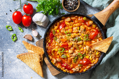 Traditional mexican food. Chili con carne from meat, beans and vegetables on dark stone table. Top view flat lay background. Copy space.