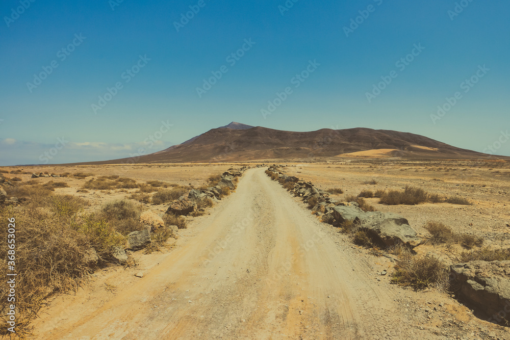 Lonely desert road through an arid landscape winds towards volcanic mountains on the horizon, seen at the Rubicon plains near Playa Blanca and the Papagayo coast, Lanzarote, Canary Islands, Spain. 
