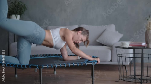 Coach does exercises for buttocks, standing on a home mini trampoline. photo