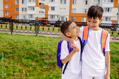 Two boy friend schoolchildren are hugging each other on the street on the way to school
