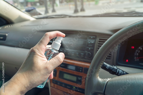 Close up hand holding alcohol spray in car. Hand sanitizer spray for clean car steering wheel and against the corona virus, covid-19, bacteria. Hand cleanser.