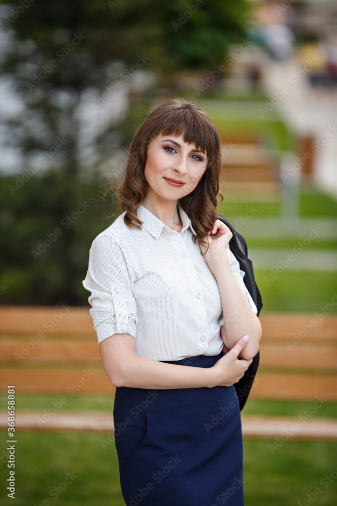 Young woman weared in classic business suit on background of a City park. Business style girl in Summer City on background of new park near a building. Street style Modern strict urban girl. Young woman weared in classic business suit on background of a City park. Business style girl in Summer City on background of new park near a building. Street style Modern strict urban girl.