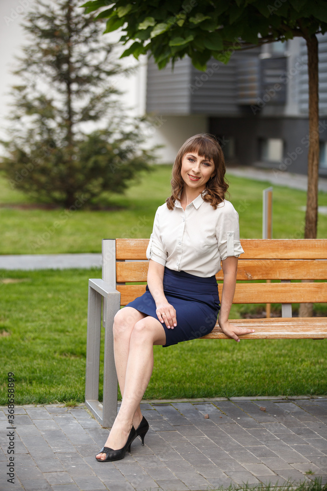 Young woman weared in classic business suit on background of a City park. Business style girl in Summer City on background of new park near a building. Street style Modern strict urban girl. Young woman weared in classic business suit on background of a City park. Business style girl in Summer City on background of new park near a building. Street style Modern strict urban girl.