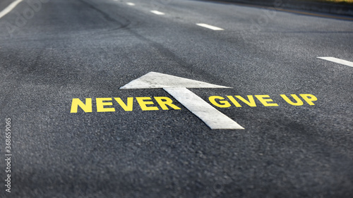 Never give up word with white arrow and dividing lines on black asphalt road, business challenge concept and effort idea