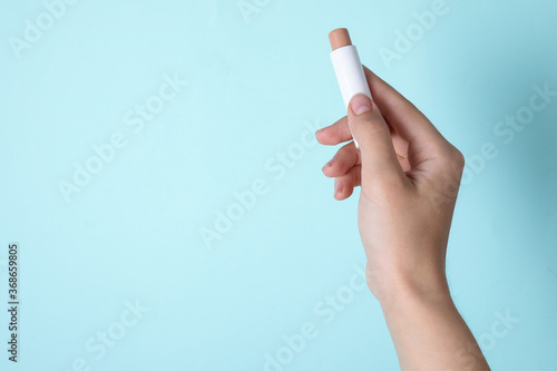 Woman holding hygienic lipstick on turquoise background, closeup. Space for text