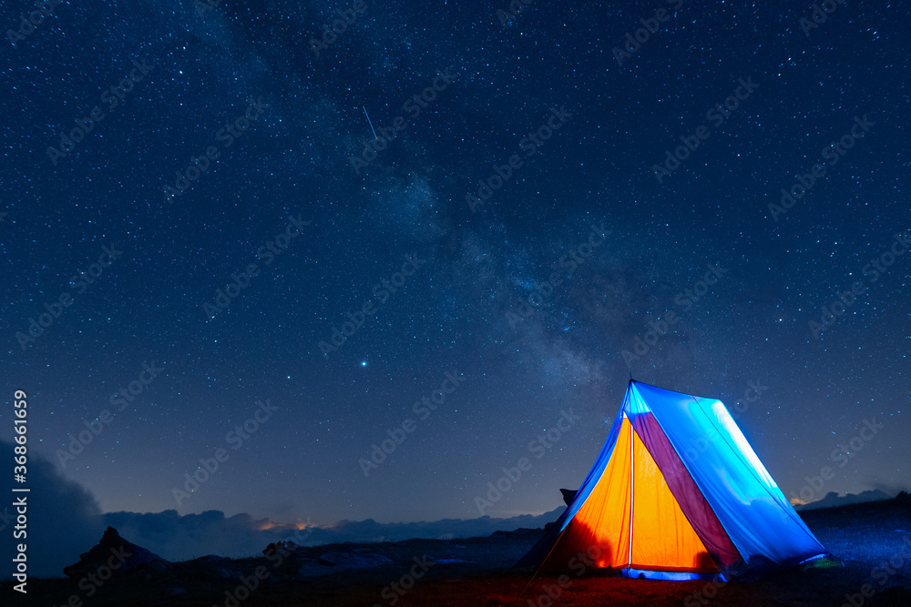 Tent glowing under the milky way at night. Camping in the mountains under the starry magical sky. 5 Billion Star Hotel.