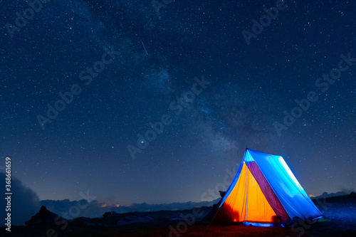Tent glowing under the milky way at night. Camping in the mountains under the starry magical sky. 5 Billion Star Hotel.