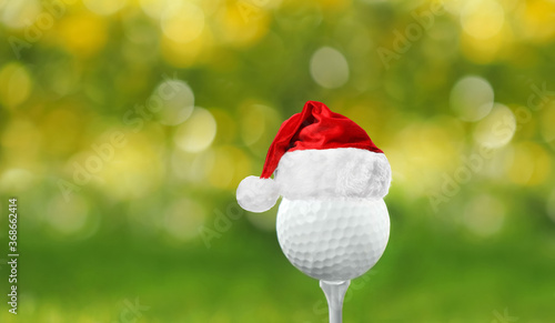 Golf ball with small Santa hat on tee against blurred background