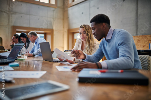 Multiethnic male and female colleagues discussing over chart while sitting at conference table during meeting at office