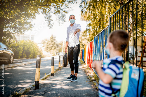 Fototapeta Naklejka Na Ścianę i Meble -  Business father and son going to kindergarten. They are wearing a medical face masks.