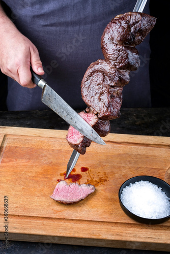 Traditional barbecue dry aged wagyu Brazilian picanha from the sirloin cap of rump beef sliced by a chef directly from the skewer as closeup on a wooden cutting board photo