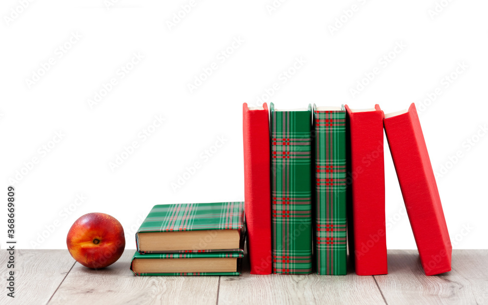 Naklejka premium Back to school, pile of books in colorful covers and red peach on wooden table with empty white background. Distance home education. Quarantine concept of stay home