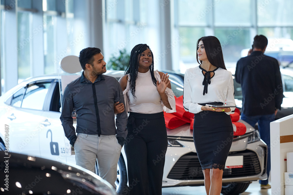 Visiting a car dealership choosing and buying a new car a young emotional African-American couple communicates in with a car sales Manager. Selective focus. Visiting a car dealership choosing and buying a new car a young emotional African-American couple communicates in with a car sales Manager. Selective focus.