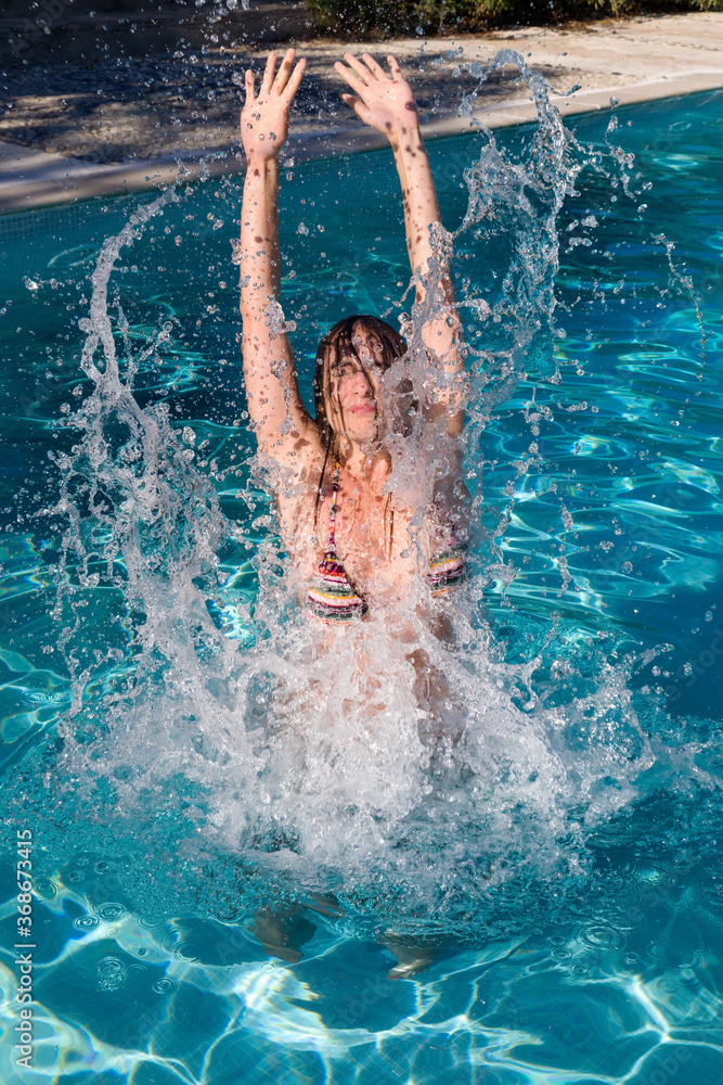 Young woman jumping into the swimming pool making a big splash