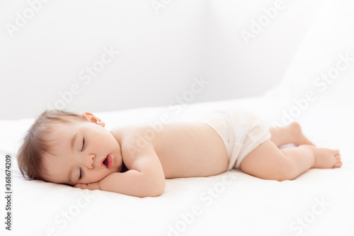 Full body shot of sleeping baby on white bed