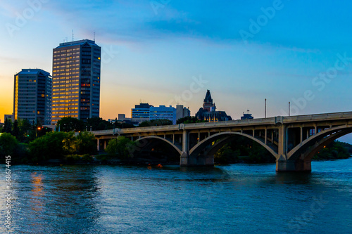 Beautiful view of the Broadway Bridge with the skyline of the City of Saskatoon in the background during a colorful sunset © Sask Photography