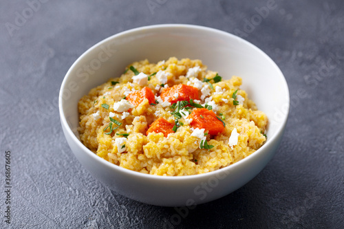 Spelt porridge with roasted pumpkin and cream cheese in bowl. Grey background. Close up.