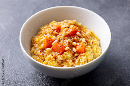 Spelt porridge with roasted pumpkin and pine nuts in bowl. Grey background. Close up.