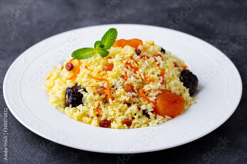 Pilaf, plov with dried fruits and saffron. Dark background. Close up.