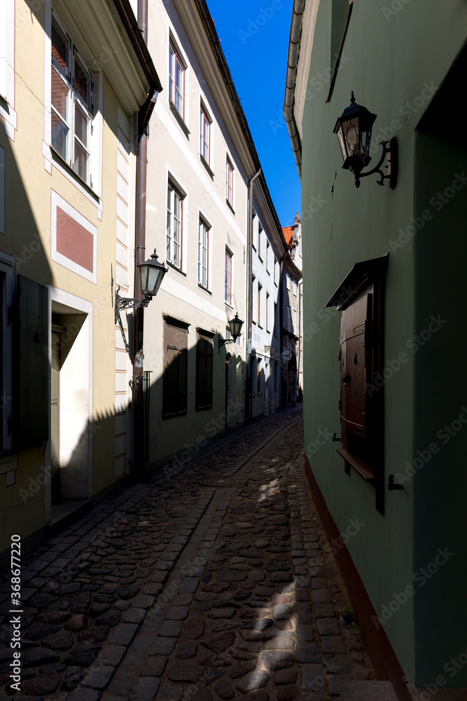 Narrow street in the old town of Riga. Blue sky between the facades of old houses with lamps.
