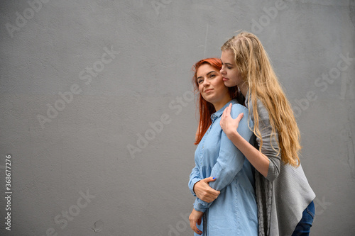 Two happy girlfriends are hugging on the background of a gray wall. Gentle hugs of a female lesbian couple. LGBT Same-sex marriage. © Михаил Решетников