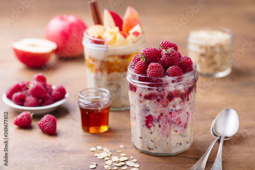 Overnight oats  bircher muesli with raspberry and apple in glass jars. Wooden background. Close up.