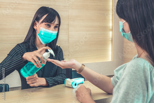 Receptionist and guest wearing face mask at front desk while having conversation in office or hospital . Covid 19 and coronavirus infection protection and protective policy concept .