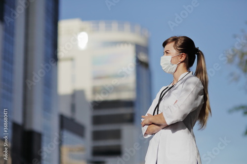 Female doctor  nurse wearing a protective face mask in the city. Skyscraper  sky