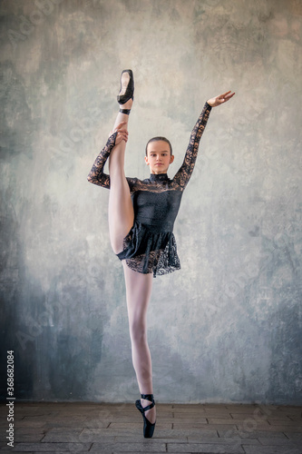 young ballerina in a black suit and black pointe shoes, dancing against the background of a textured wall, froze in a graceful pose