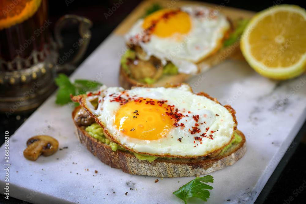 Fried egg sandwich with avocado and mushrooms.