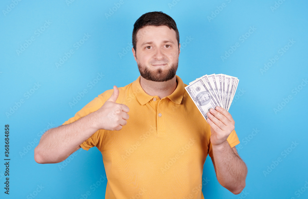 Φωτογραφία Brunette pleased man holding pile of paper money, showing thumb up