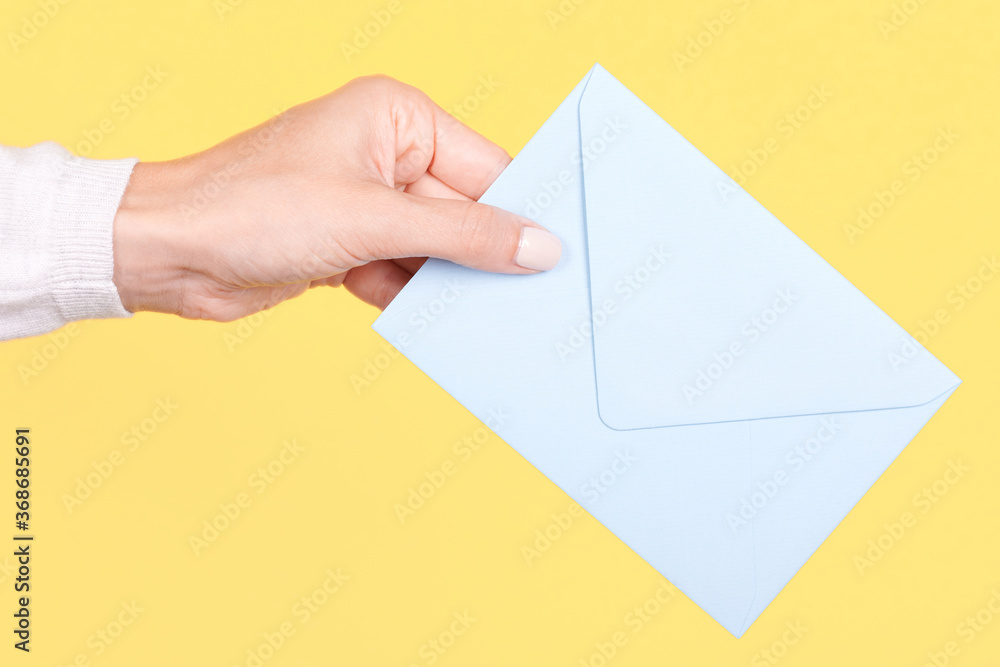 Hand with blue paper envelope. Isolated on yellow background.