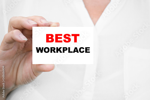 Closeup on business woman holding a card with BEST WORKPLACE message, business concept image with soft focus background
